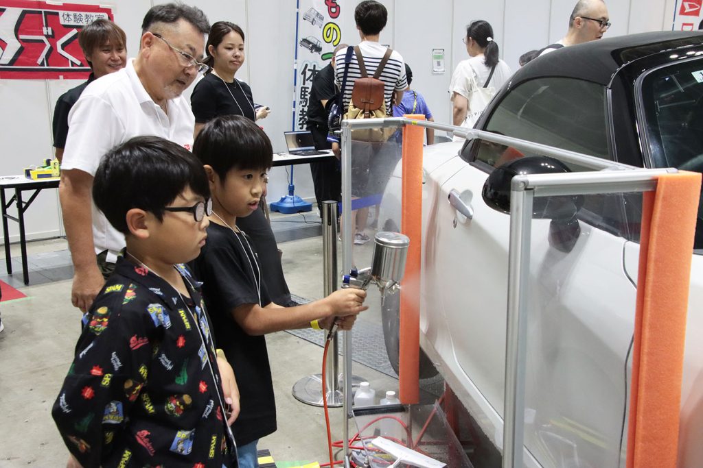 「塗装」工程でコペンGRスポーツのドアに水を吹き付ける様子。スプレーガンはトラスコ-デビルビスTSG-508を使用